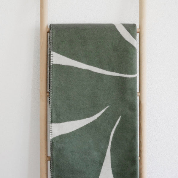 XL Kuscheldecke BJÖRK mit großem, grünem, floralem Motiv gefaltet auf Leiter