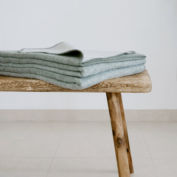 XL Kuscheldecke in grün aus recycelter Baumwolle, auf einer Holzbank