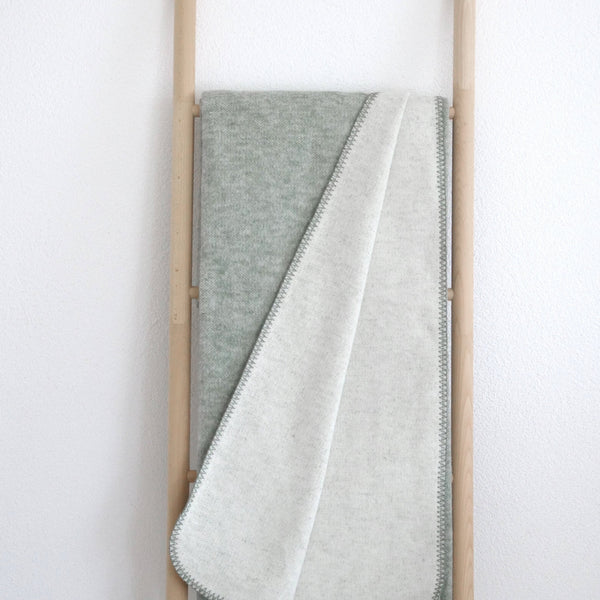 XL Kuscheldecke in grün aus recycelter Baumwolle, auf einer Holzleiter