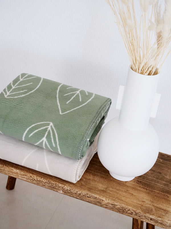 warme kuscheldecken in grün und beige aus bio baumwolle auf holzbank mit Vase