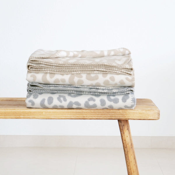 RIEMA XL Kuscheldecke aus recycelter Baumwolle mit Leo Muster in beige und grau auf Holzbank